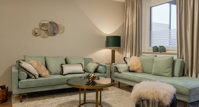Gemütliches Wohnzimmer mit grünen Sofas und goldenen Akzenten.