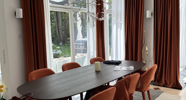 Essbereich mit runden Stühlen in Terrakotta und deckenhohen Vorhängen.