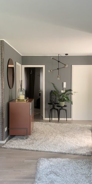 Modern eingerichtetes Wohnzimmer mit gemusterter Tapete und offener Küche.