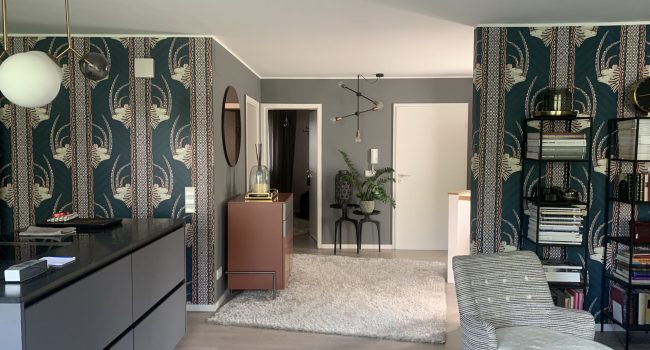 Modern eingerichtetes Wohnzimmer mit gemusterter Tapete und offener Küche.