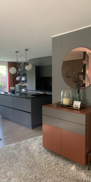 Blick auf die moderne Küche mit dunklen Fronten und dekorativer Kommode mit Spiegel.