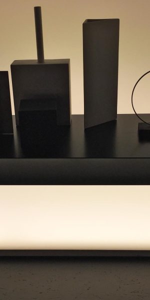 Minimalistischer schwarzer Tisch mit geometrischen Objekten vor indirekter Beleuchtung