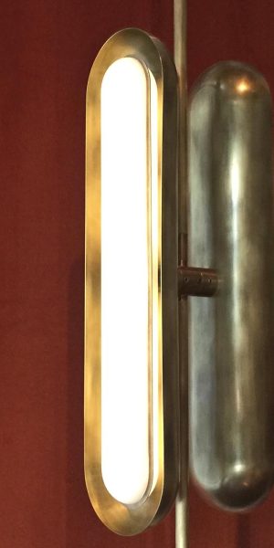 Nahaufnahme einer vertikalen Wandleuchte mit abgerundetem Design in goldener Metallausführung.